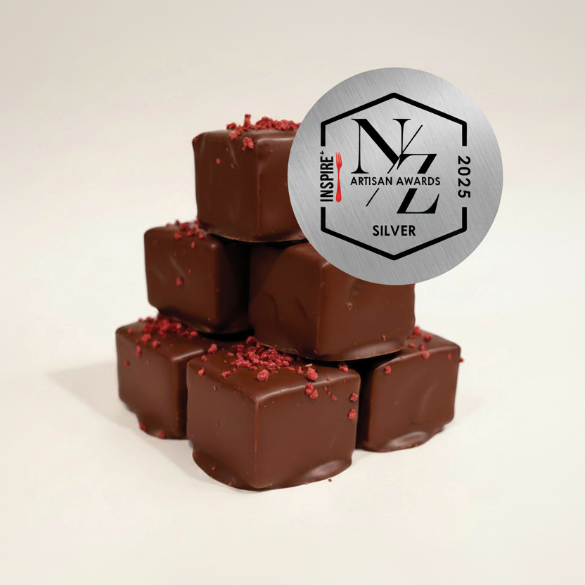 Stack of chocolate candies with red sprinkles and a silver 'Inspire Artisan Awards 2025 Silver' badge on a beige background.